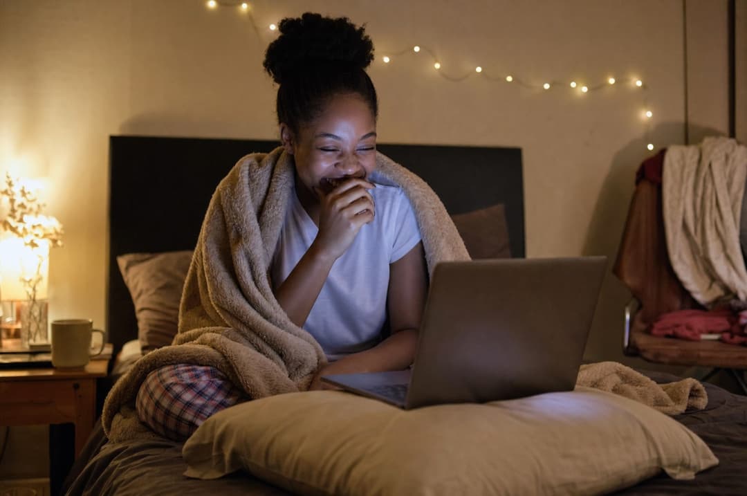 Amara in bed at night, laughing at her laptop